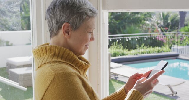 Senior Woman Using Smartphone by Window Overlooking Garden Pool - Download Free Stock Images Pikwizard.com