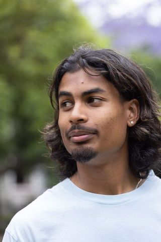 Indian man standing in park wearing light blue t-shirt and stud earring, contemplative headshot