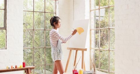 Young Woman Painting in Bright Art Studio with Large Windows