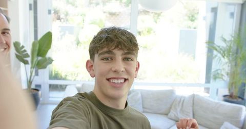 Teenage boy smiling and taking selfie in bright modern living room with sectional sofa