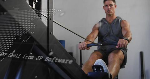 Male athlete performing intense indoor rowing workout on ergometer for strength training