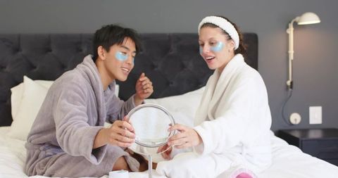 Couple applying under-eye patches wearing plush robes sharing cozy skincare moment