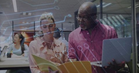 Mentor reviewing project with colleague using laptop and folder, digital circuit overlay