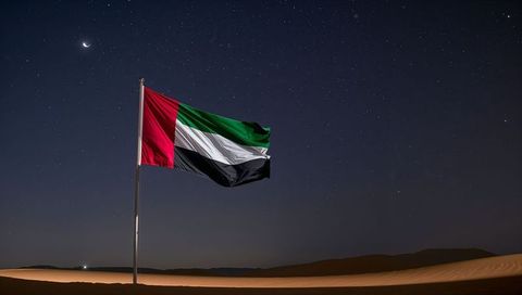 Waving uae flag over moonlit arabian desert dunes with crescent starry sky and flagpole