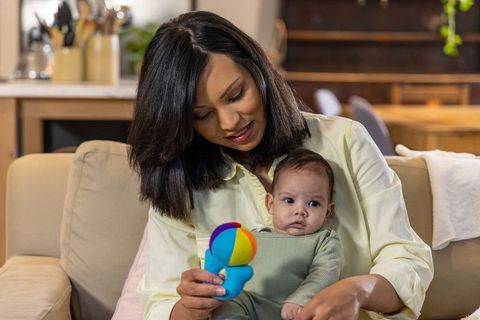 Indian mother bonding with infant girl on sofa while showing colorful plush toy at home