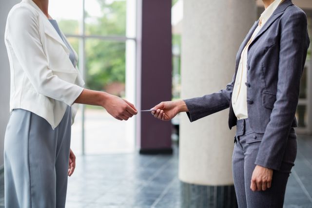 Two business executives are exchanging business cards in a modern conference center. This image can be used to illustrate networking events, professional meetings, corporate introductions, and business partnerships. It is ideal for business-related articles, corporate websites, and promotional materials for networking events.