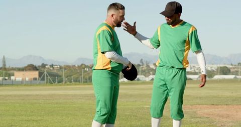 Cricket teammates discussing tactics on outfield wearing green and yellow uniforms