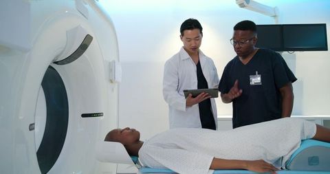 Diverse medical team consulting on tablet while preparing female patient for ct scanning