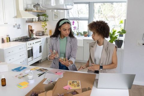 African american women collaborating on skincare packaging and branding in home kitchen