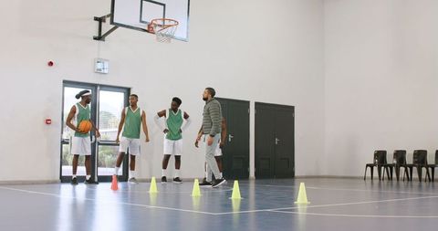 Basketball Coach Guides Players Through Cone Drill in Indoor Gymnasium