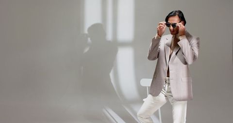 Stylish asian man adjusting sunglasses in bright studio