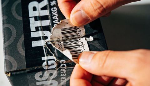 Peeling torn barcode sticker from black shoebox closeup hands removing label
