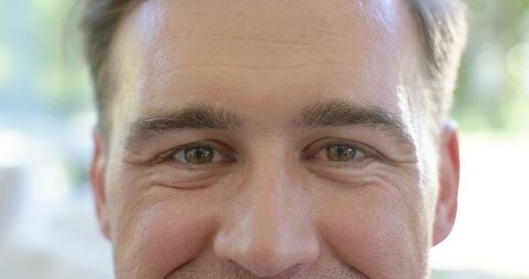 Closeup adult male face smiling and gazing, soft natural window light, gentle stubble