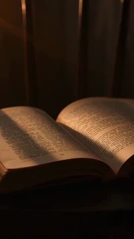 Warm lamp beam sweeping across open book on wooden table vertical video for moody study