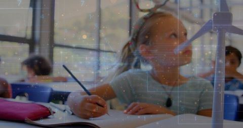 Elementary student writing notebook while observing wind turbine model for stem learning