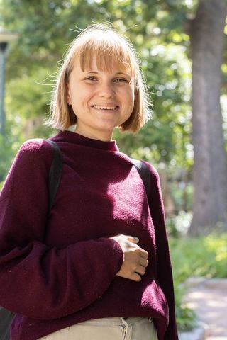 Smiling young woman in burgundy sweater carrying backpack on sunlit park path
