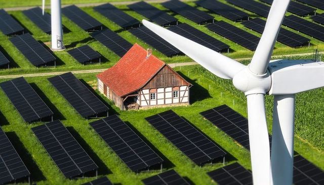 Timber-framed farmhouse sitting among solar panel arrays and wind turbine on green farmland