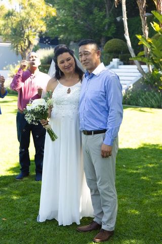 Mature couple posing after garden wedding while guest blowing bubbles in sunlight