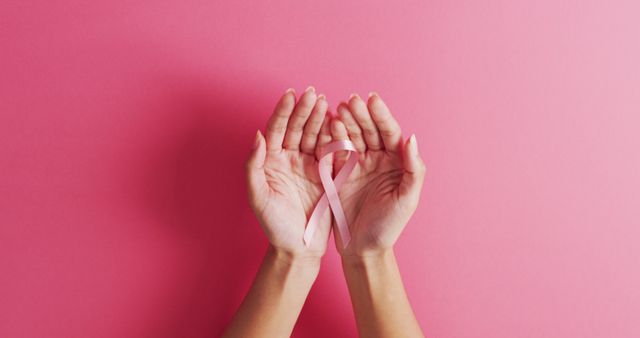 Image of hands of caucasian woman holding pink ribbon on pink background. medicine, health, cancer awareness concept digitally generated image.