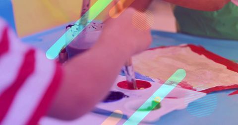 Young boy painting with watercolor palette at colorful classroom art table for kids