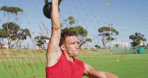 Athletic man lifting kettlebell overhead on park field with red digital grid overlay