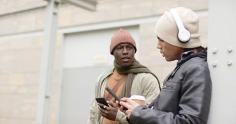 Young diverse friends chatting and checking smartphones with coffee in urban streetwear