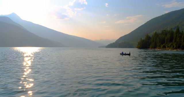 People canoeing on calm mountain lake at sunset creating a serene and peaceful scene. Great for promoting adventure tourism, nature relaxation, outdoor activities, and travel programs.