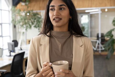 Indian businesswoman holding mug and speaking in modern coworking office