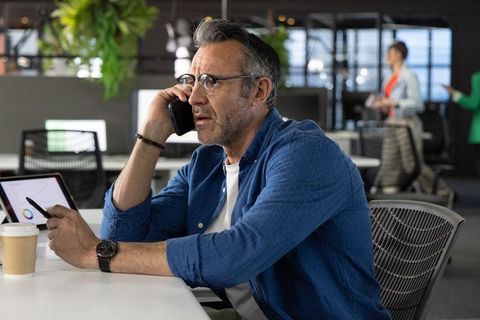 Mature professional making business call while reviewing tablet analytics in modern office