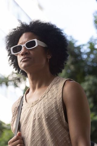 Walking urban african american man wearing white sunglasses and beige textured tank top