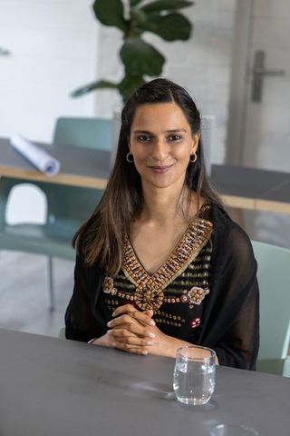 Indian businesswoman sitting at conference table wearing embroidered black tunic smiling