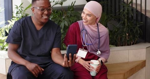 Diverse healthcare team sharing smartphone and coffee during break in hospital lobby