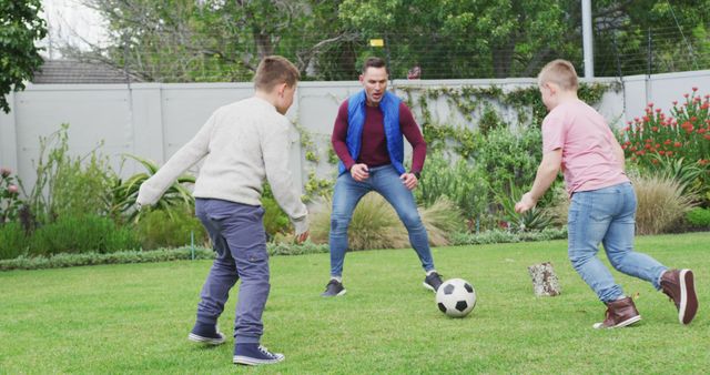 Happy caucasian father with two sons playing football in garden. family spending time at home.