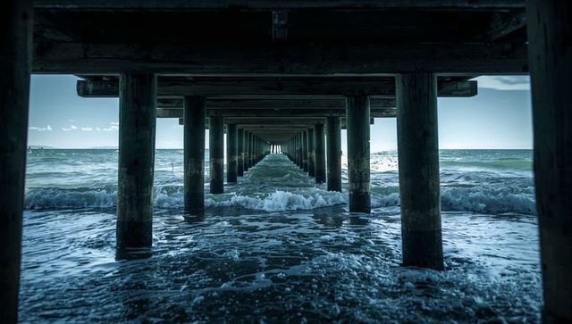 Framing under-pier tunnel revealing wooden pilings leading to ocean horizon