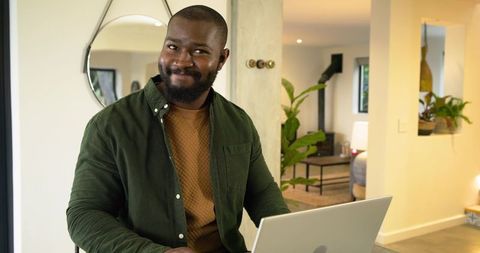 African American man working on laptop in modern home office with plants and mirror
