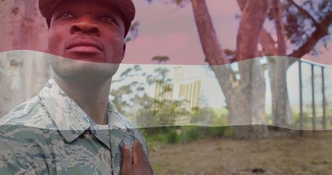 Stoic soldier standing in woodland placing hand over chest with egyptian flag overlay