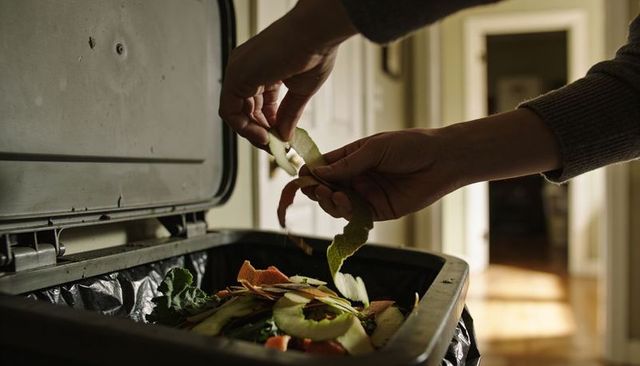 Hands dropping vegetable peels into kitchen compost bin for sustainable home waste