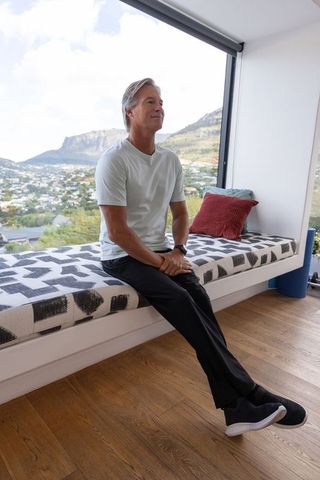Senior man sitting on window bench gazing at mountain valley view in minimalist interior