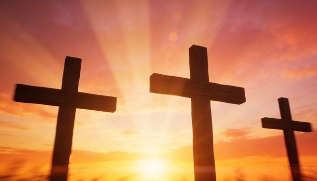 Three wooden crosses on hill at sunrise with golden rays and dramatic silhouette