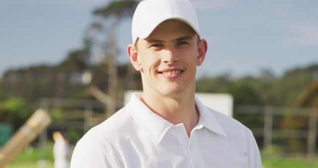 Portrait of happy caucasian male cricket player wearing cap on field. Cricket, sports, match and active lifestyle, unaltered.