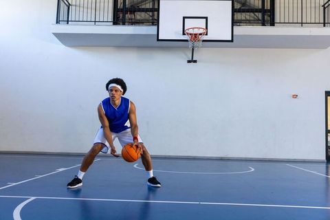 Focused African American Teen Dribbling Basketball on Indoor Court