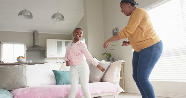 This image shows a joyful moment with a mother and her daughter dancing together in a living room. Perfect for use in family-oriented content, parenting articles, advertisements promoting home happiness, or any content emphasizing bonding and togetherness between a parent and child.
