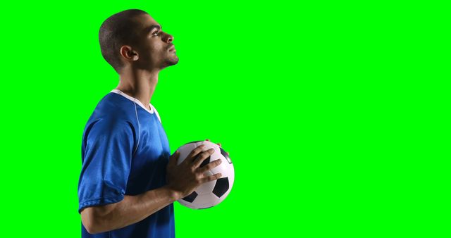 Man holding soccer ball while gazing upwards against a green background, focused and in deep thought, can be used for sports promotion, athlete motivation, or green screen editing for various backgrounds.