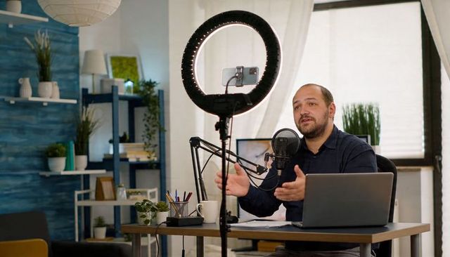 Male Creator Speaking and Gesturing Recording Podcast in Home Studio with Ring Light Mic