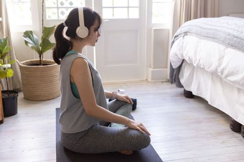Woman practicing meditation on yoga mat in sunny bedroom wearing headphones