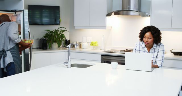 Woman Using Laptop at Modern Kitchen Counter While Man Prepares Meal - Download Free Stock Images Pikwizard.com