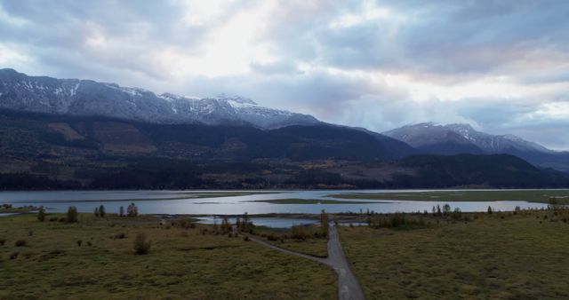 A serene landscape showcases a mountain range and a lake at dusk. The winding path adds a sense of journey amidst the tranquil outdoor setting.