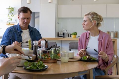 Young couple sharing healthy salad at modern wooden dining table while enjoying conversation