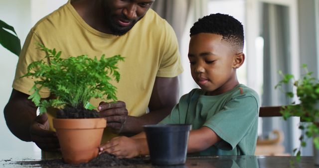 African american boy adding new soil to the plant pot at home. family father son togetherness relationship concept