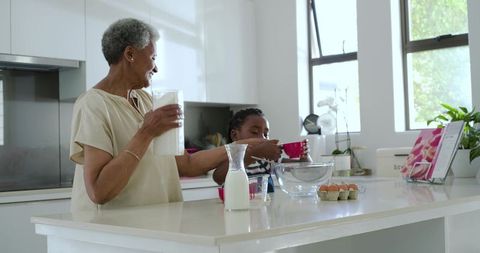 Senior african grandmother and granddaughter baking together on bright white kitchen island